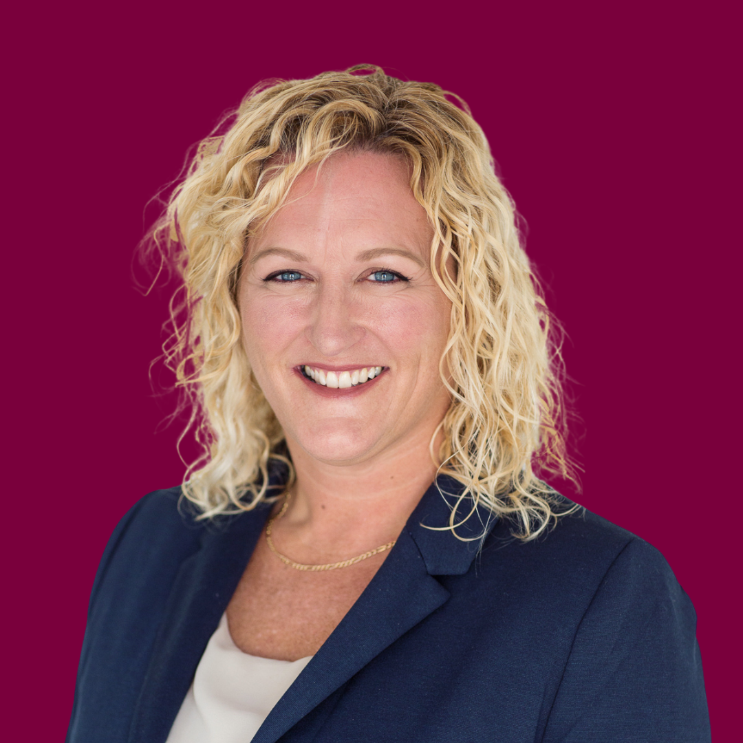 Portrait of Tanya Elliot, a smiling woman with curly blonde hair, wearing a navy blazer.